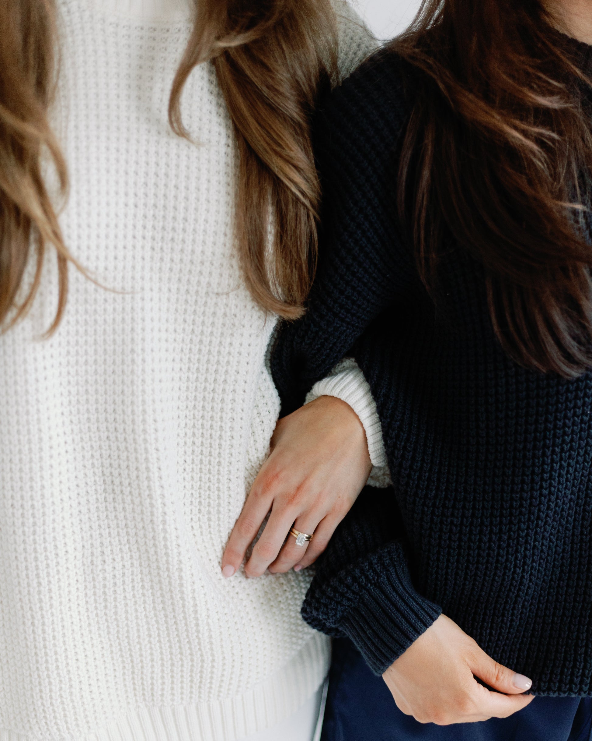 Two people wearing white and navy sweaters with a neutral background
