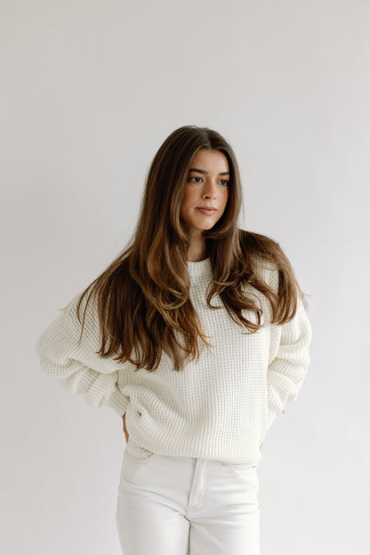 Woman wearing a white sweater and pants against a plain background